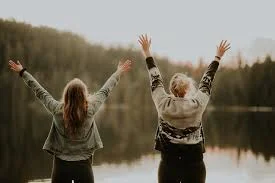 Niñas con los brazos en alto en un campo abierto, celebrando la felicidad.